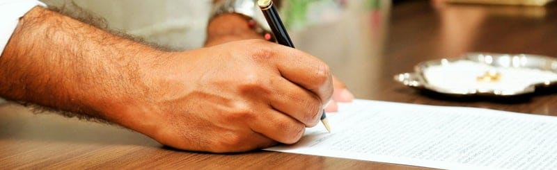 Hand signing a document with a fountain pen on a wooden table